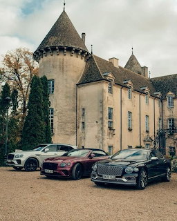 Three Bentley cars parked in front of a historic stone chateau