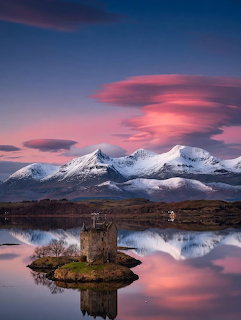 Small stone tower on a lake island with snowy mountains and pink clouds reflected in still water