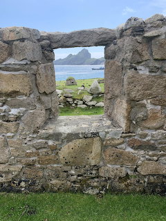 View through ancient stone wall window opening showing green fields and a rocky sea stack island in the distance