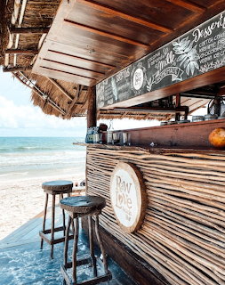 Rustic tiki bar with stools beside a sandy beach and calm ocean