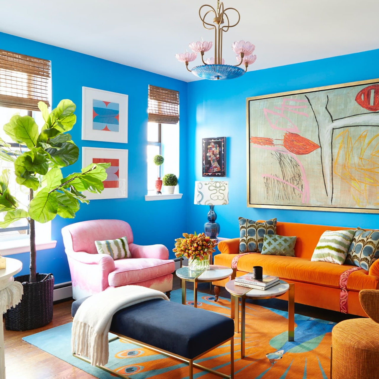 Colorful living room with blue walls, pink chair, orange sofa, plants, and wall art