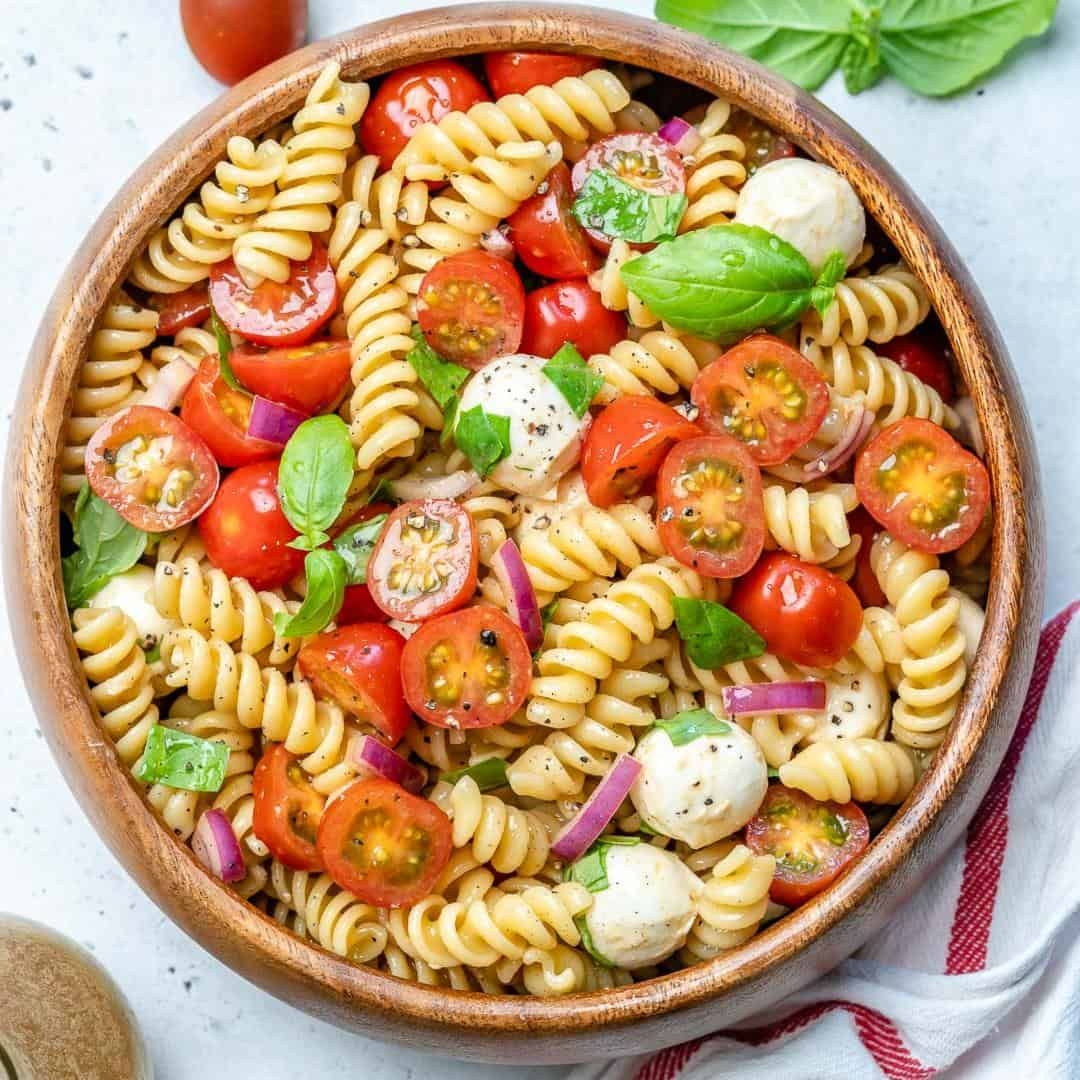Overhead view of rotini pasta salad with cherry tomatoes, mozzarella, basil, and red onion in a bowl