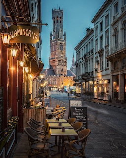 Evening street view of Bruges with illuminated Belfry tower and cafe terraces