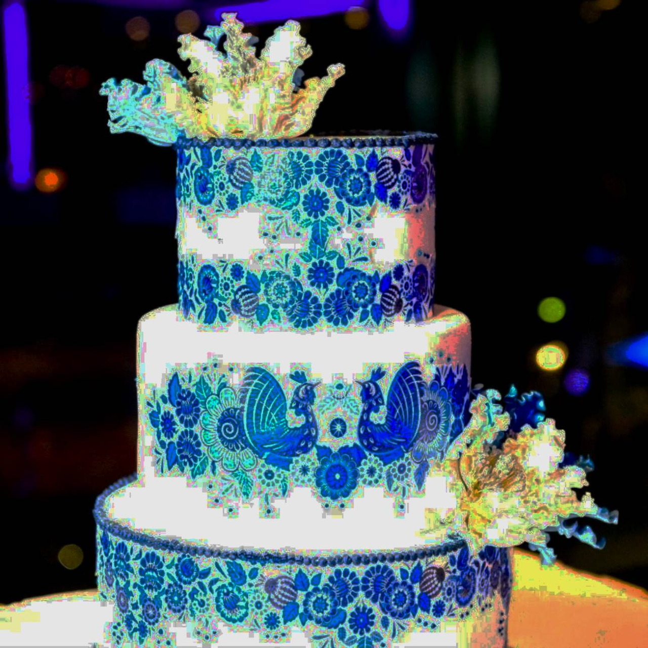 Three-tier white wedding cake with ornate blue baroque lace patterns and white floral decorations on top