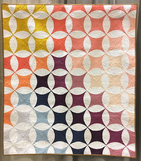 Geometric quilt with overlapping circles in warm and cool colors forming a gradient pattern on cream fabric