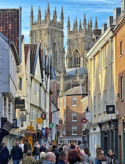 Pedestrians on a narrow Lincoln street with Lincoln Cathedral towers behind historic buildings