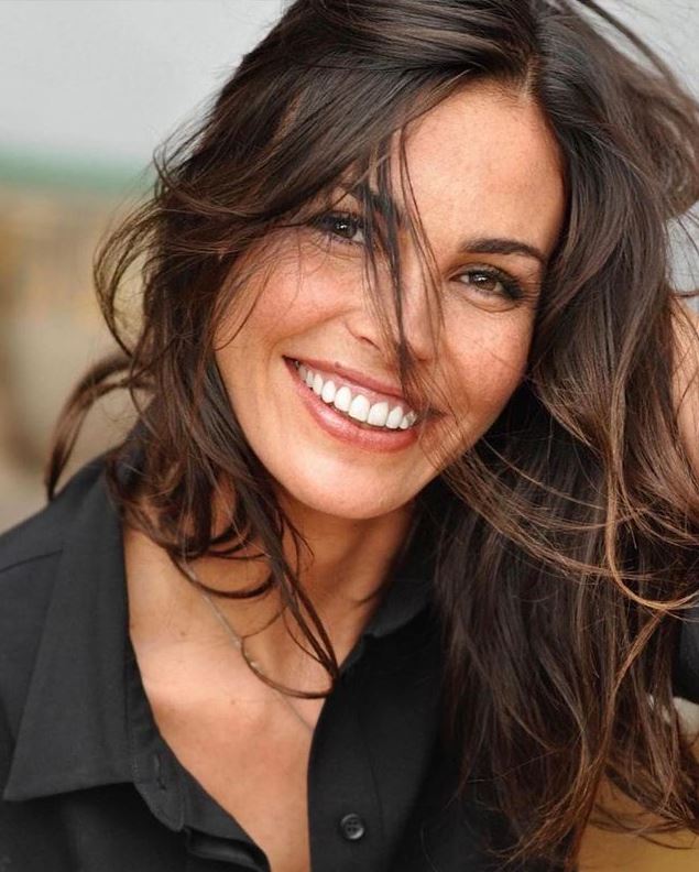 Close-up portrait of a smiling brunette woman with windblown hair wearing a black shirt
