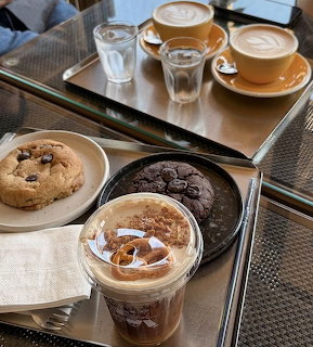 Top-down cafe table with two lattes, an iced coffee, chocolate chip cookie, and chocolate cookies on a tray