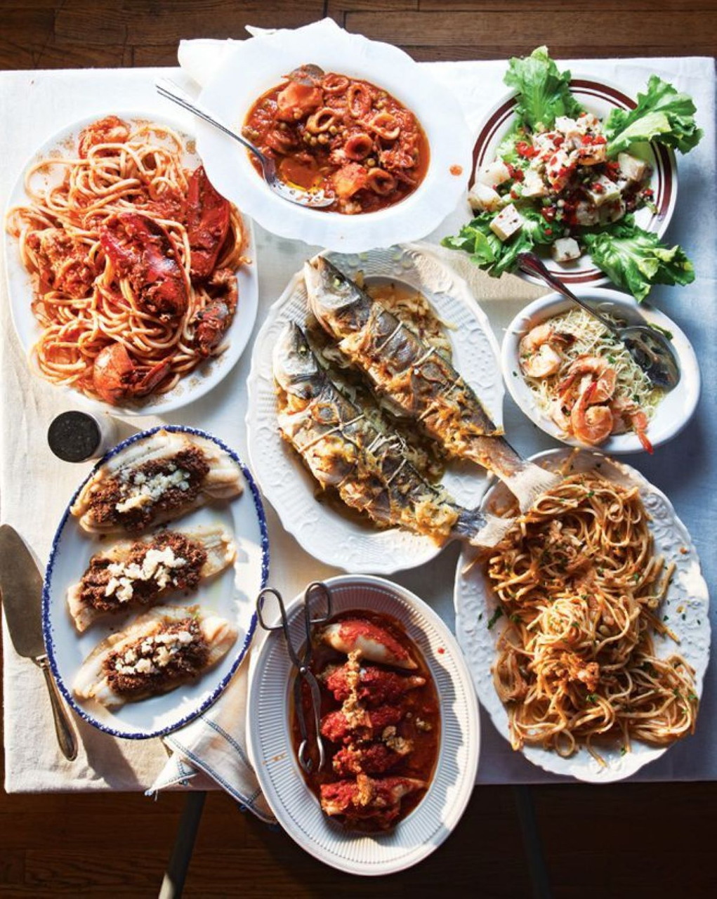 Overhead view of Italian seafood dishes including pasta, grilled fish, mussels, and salad on white plates