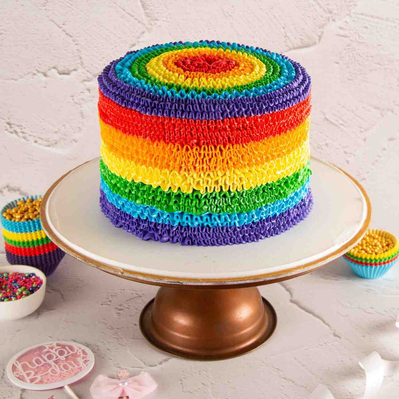 Rainbow layer cake with colorful buttercream frosting on gold stand