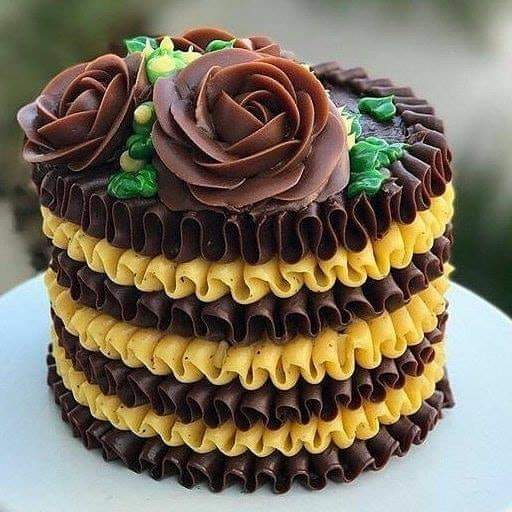 Three-layer chocolate cake with yellow and brown frosting ruffles, decorated with chocolate roses and green leaves on top