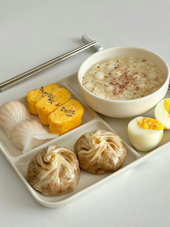Tray of Korean-style food with porridge, dumplings, sliced egg roll, garlic, and a boiled egg