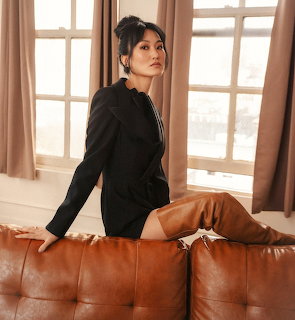 Woman in black top sitting on brown leather sofa near window with sheer curtains