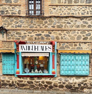 Stone building in Toledo with turquoise shutters and window display showing antique items