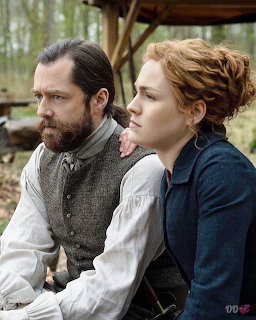 Bearded man and red-haired woman in historical costumes sitting outdoors from Outlander TV series