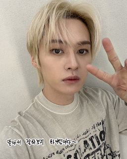 K-pop idol Lee Know with blonde hair making peace sign, wearing gray shirt