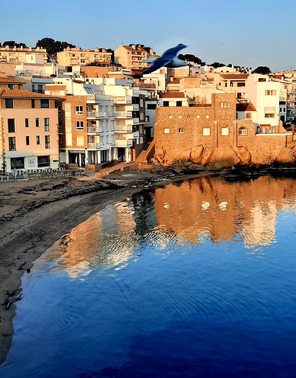 Sunset view of coastal town with orange buildings reflecting in blue water