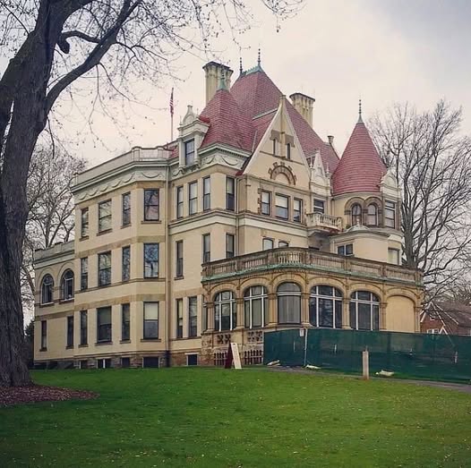 Victorian mansion with red conical turret roofs and ornate yellow stone facade surrounded by bare winter trees