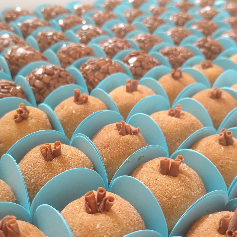 Multiple rows of round Brazilian paçoquinha candies in blue paper cups with peanut topping