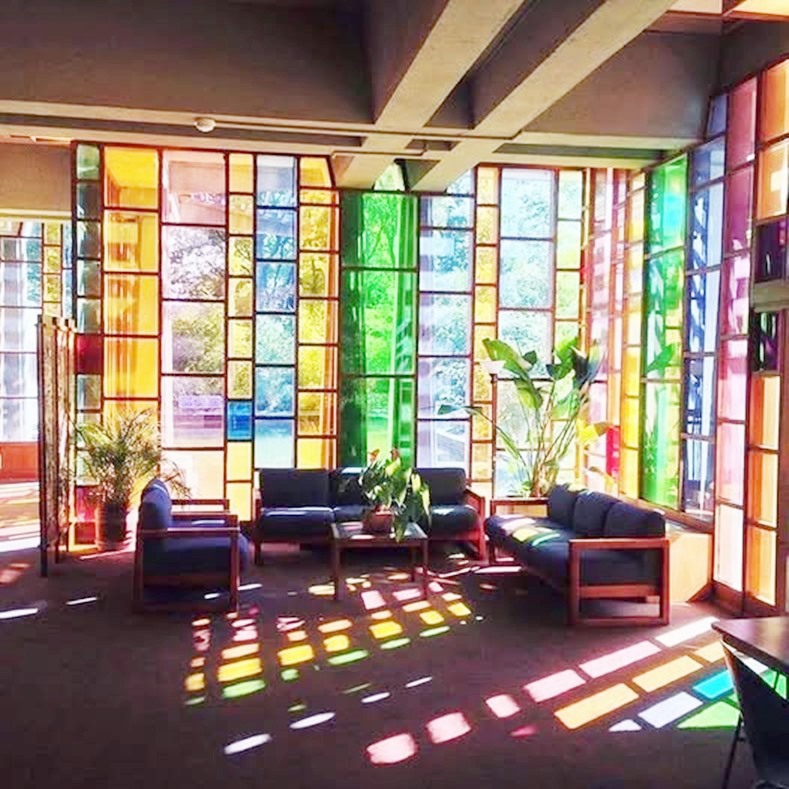 Sunlit lobby with tall stained glass windows creating rainbow light reflections on floor and furniture