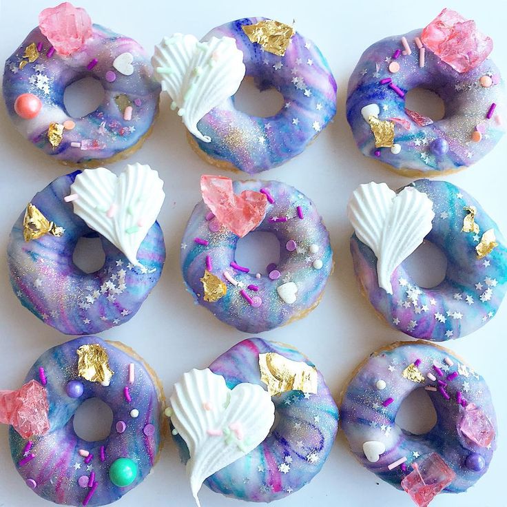 Nine doughnuts with purple-blue galaxy icing, decorated with white seashells and gold accents