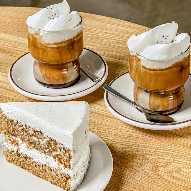 Two Vienna lattes with whipped cream and a slice of vanilla layer cake on white plates