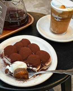 Tiramisu dessert on white plate with iced coffee and teapot on dark table