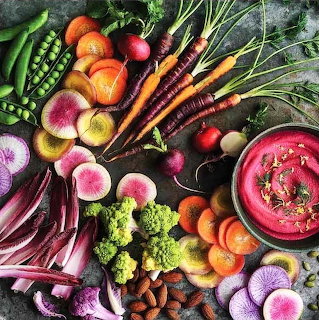 Colorful assortment of fresh organic vegetables including carrots, beets, radishes, and greens arranged on dark table