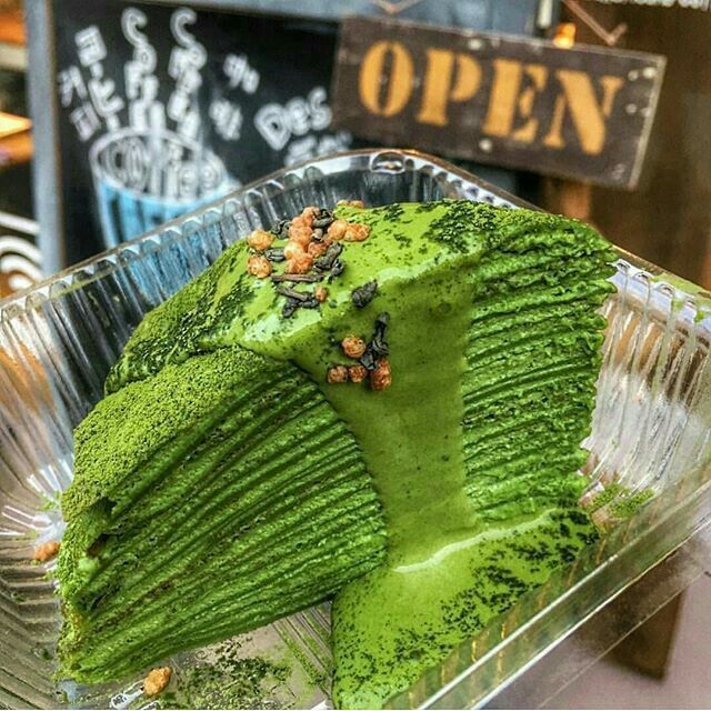 Slice of matcha crepe cake with many thin green layers in a clear plastic container