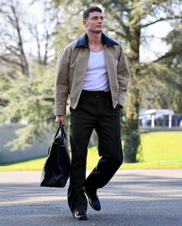 Benjamin Pavard walking outdoors wearing a beige jacket, white t-shirt, black trousers, holding a dark bag