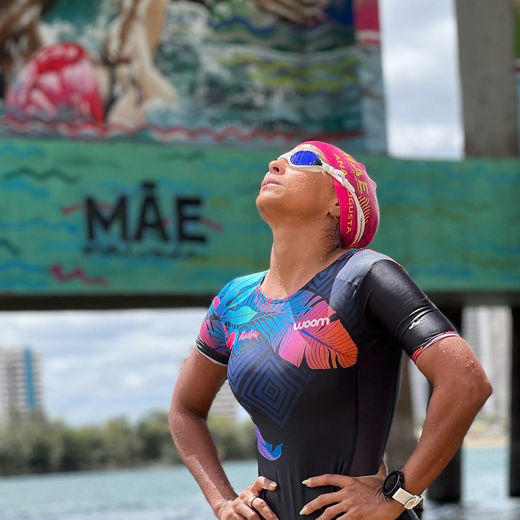 Female triathlete in wetsuit and swim cap standing by the water outdoors