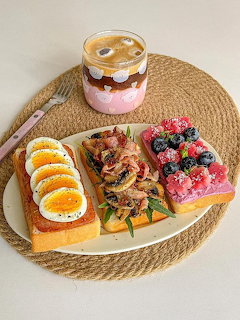 Three open-faced toasts with eggs, mushrooms, and berries on a plate next to iced coffee on a woven mat