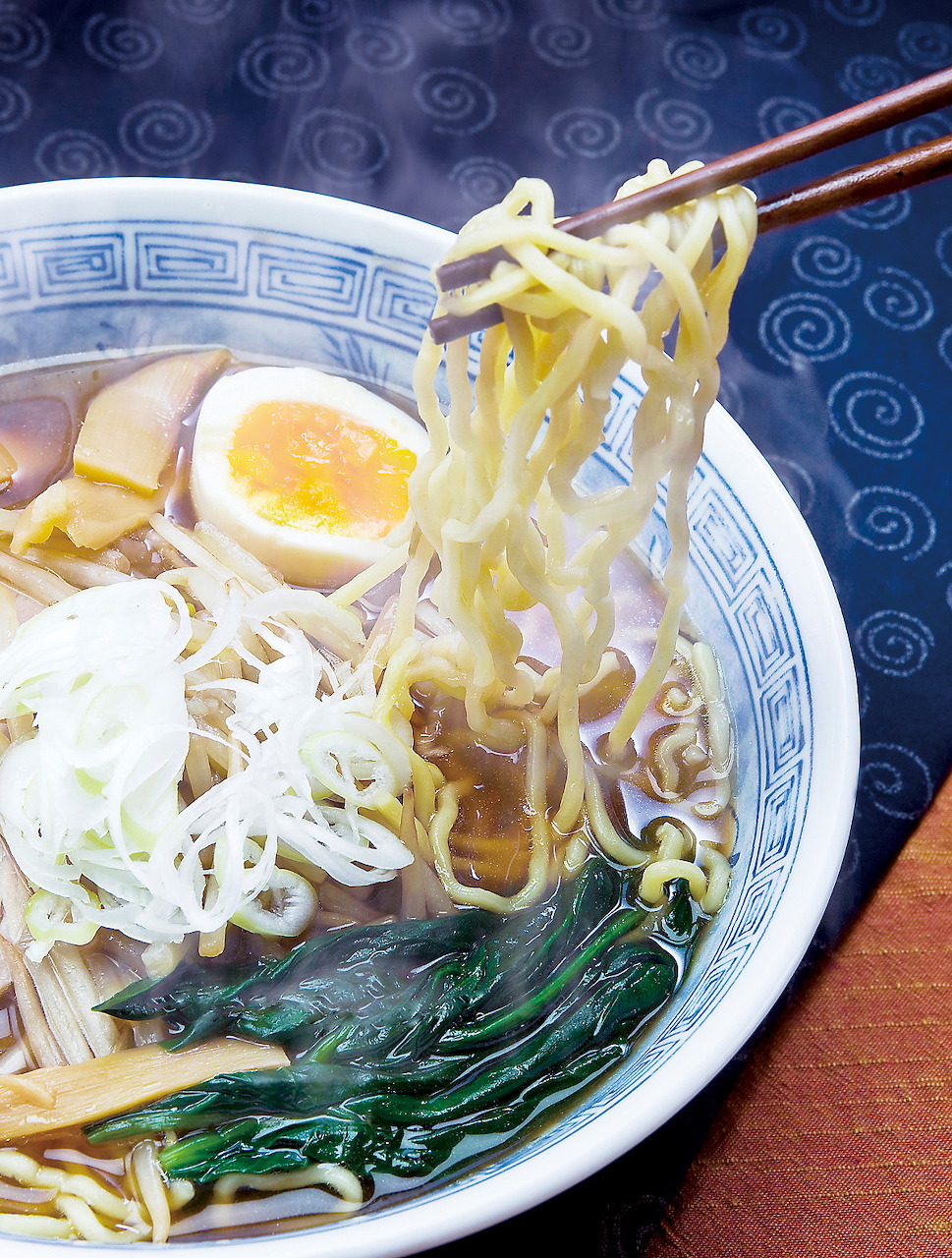 Chopsticks lifting noodles from a Japanese ramen bowl with egg, seaweed, and bean sprouts