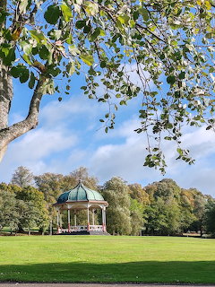 Domed bandstand on a green lawn in a Scottish park with trees and blue sky