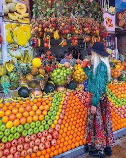Woman in boho dress and hat shopping at a colorful tropical fruit market stall