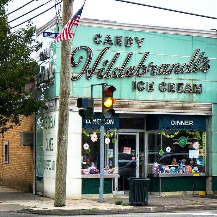 Turquoise vintage ice cream and candy shop on street corner with retro sign and American flag
