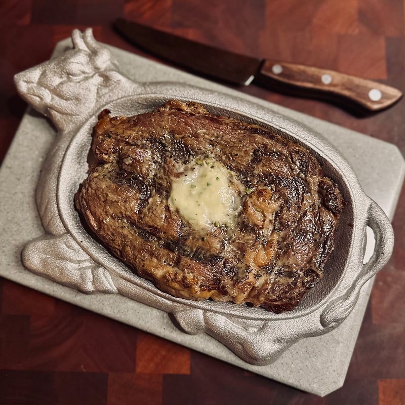Grilled ribeye steak topped with garlic butter on a white platter with a steak knife beside it