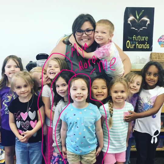 Teacher and young children posing together indoors with pink marker circles drawn over the image