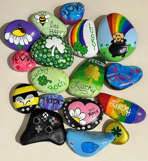Collection of painted rocks with affirmations and colorful designs including daisies, rainbows, and ladybugs