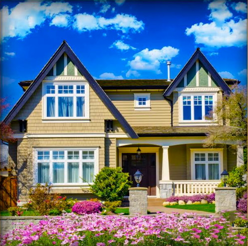Two-story craftsman house with pink flower garden, green lawn, and blue sky