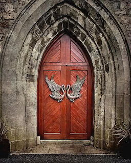 Red Gothic arched wooden door with decorative silver swan door handles in a stone archway