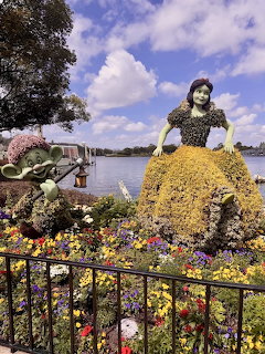 Large topiary sculpture of Snow White made of yellow and colorful flowers at Epcot with lake and sky backdrop