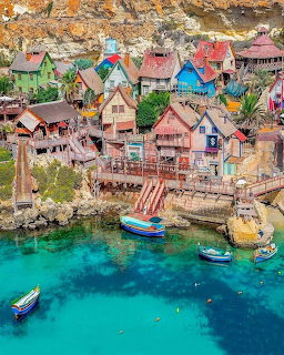 Aerial view of colorful Popeye Village in Malta with wooden houses and boats in turquoise harbor