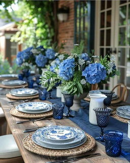 Elegant table setting with blue hydrangeas, white and blue plates, wicker chargers, and blue glassware