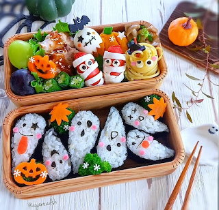 Two kawaii Halloween bento boxes with decorated rice balls, vegetables, and cute food faces on a table.