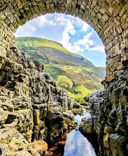 Mountain hillside and stream seen through a stone arch with rocky walls