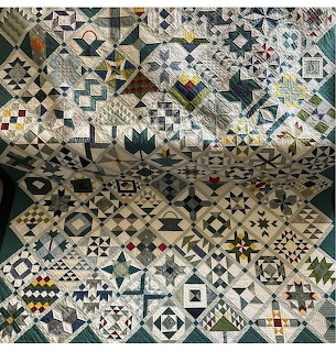 Detailed sampler quilt with varied geometric blocks in cream, black, teal, and gold fabrics draped on display