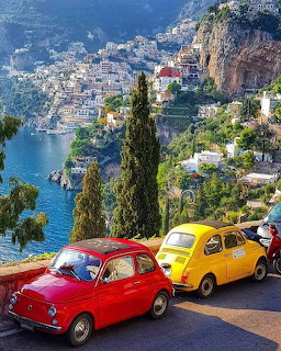 Red and yellow vintage Fiat 500 cars parked on a hillside with Amalfi Coast town and sea in background