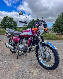 Vintage purple Suzuki GT750J motorcycle parked on a gravel road under cloudy skies
