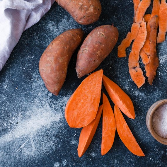 Whole and sliced sweet potatoes on a dark surface